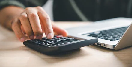 Person using a calculator next to a laptop on a desk
