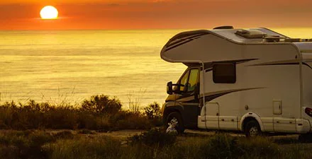 RV parked by the ocean at sunset, overlooking a scenic view.