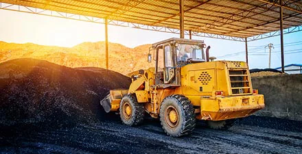 Yellow front loader moving piles of black gravel under a large metal canopy.