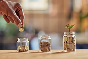 Hand placing coins in jars representing stages of financial growth.