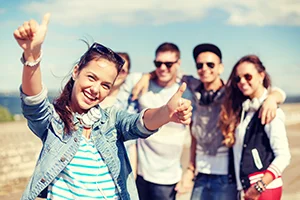 Group of happy young adults posing outdoors with one giving thumbs up.
