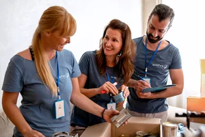 Three volunteers smiling while packing supplies together.