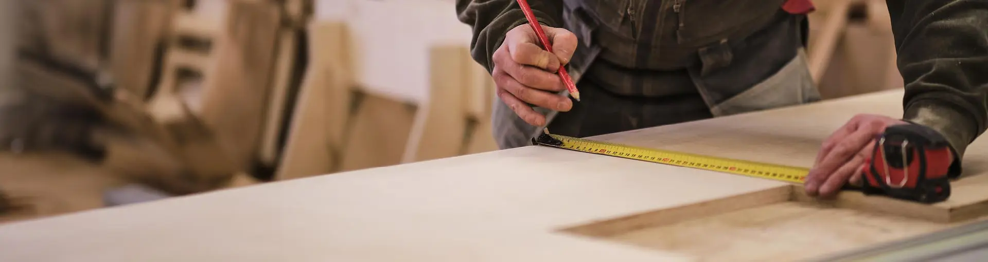 Person measuring and marking wood with a tape measure and pencil in a woodworking or carpentry workshop.