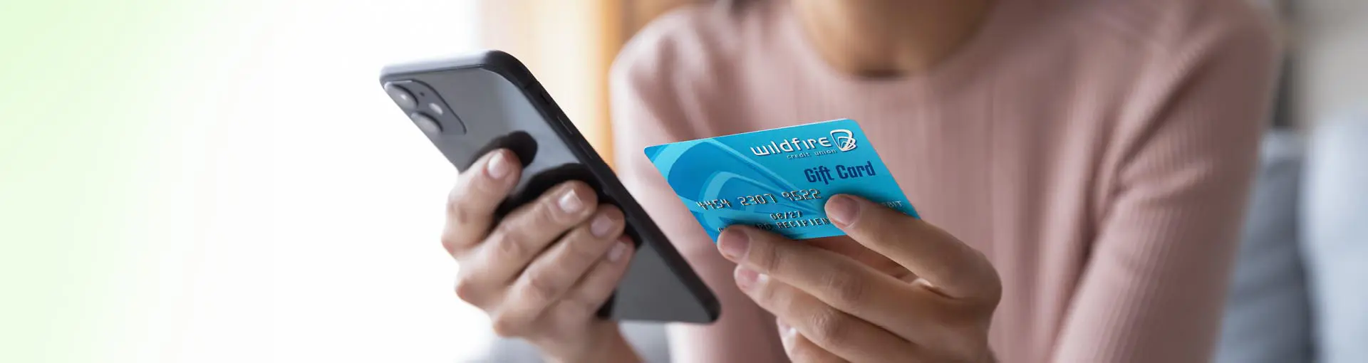 Person holding a smartphone and a blue Wildfire Credit Union gift card.