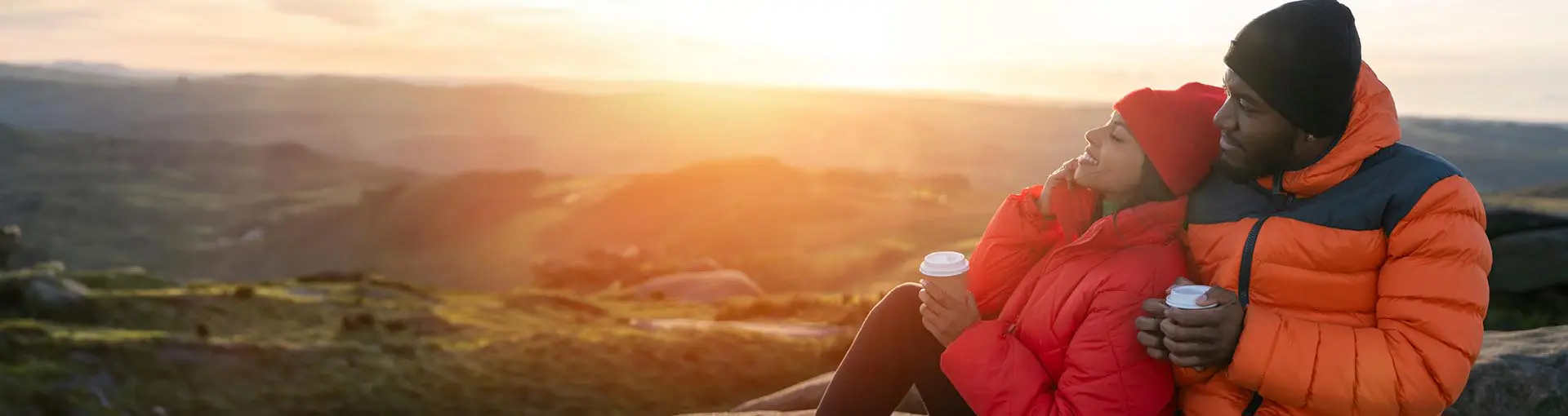 A couple sitting on top of a mountain drinking coffee looking over the scene.