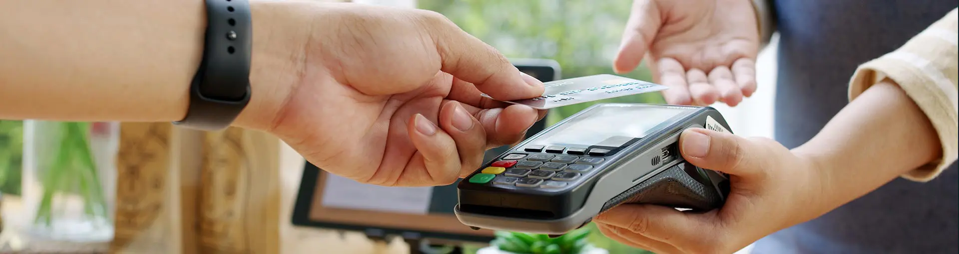 Customer taps credit card on payment terminal for contactless transaction, while cashier holds the device steady.