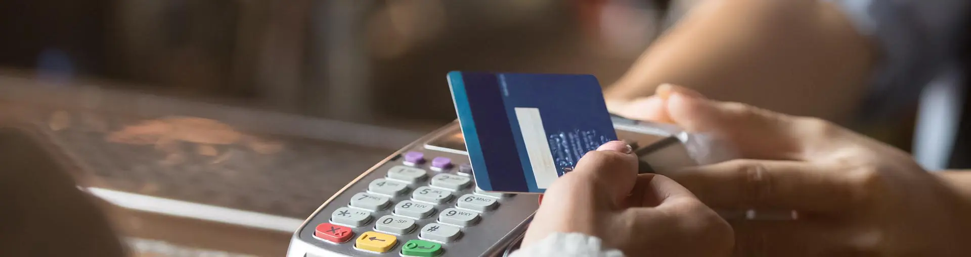 Person holding a credit card over a payment terminal to make a contactless transaction.